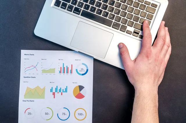 Overhead view of a business workspace with a laptop and colorful data charts on paper. Digital marketing career path: 3 stages, proof for each