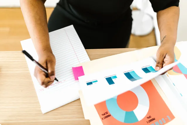 Businesswoman writing notes while analyzing printed graph reports at a desk. How to meet digital marketing job requirements