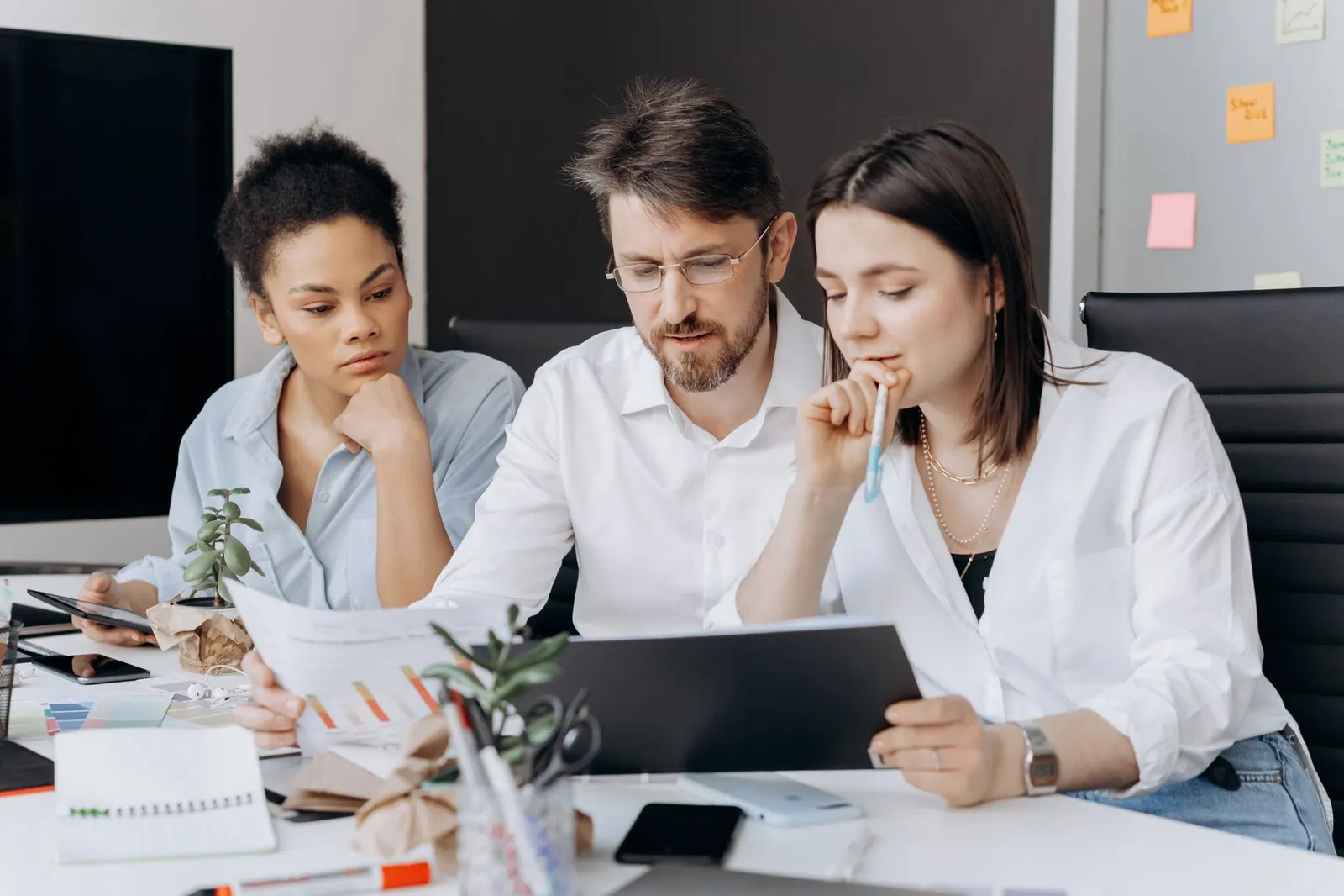Three coworkers collaborating on a project at a modern office desk with charts and laptops. Digital marketing skills, tested against experience